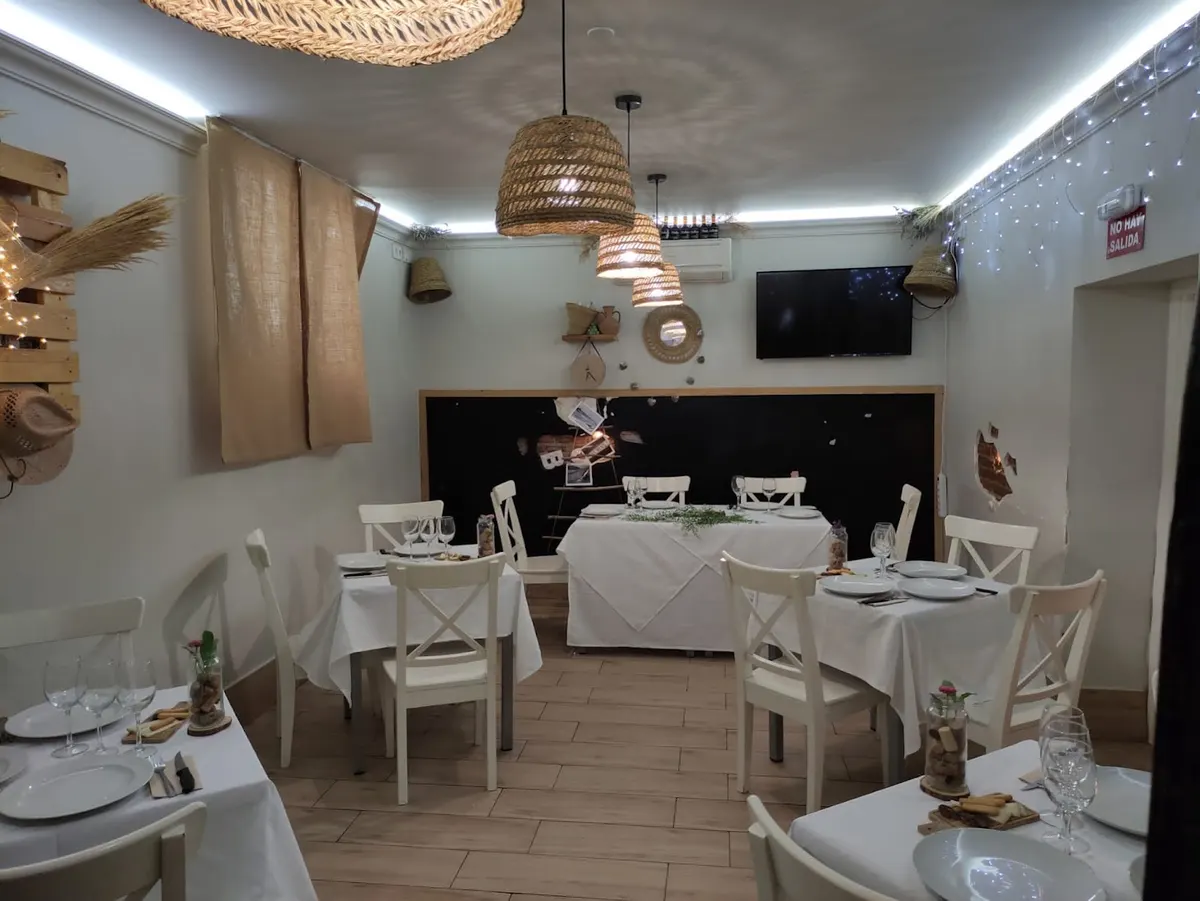 Comedor con mesas de mantel blanco, sillas blancas y lámparas de mimbre