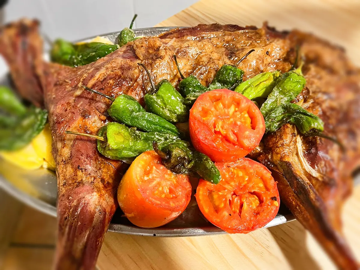 Cordero asado en fuente de horno con pimientos verdes fritos y tomates asados